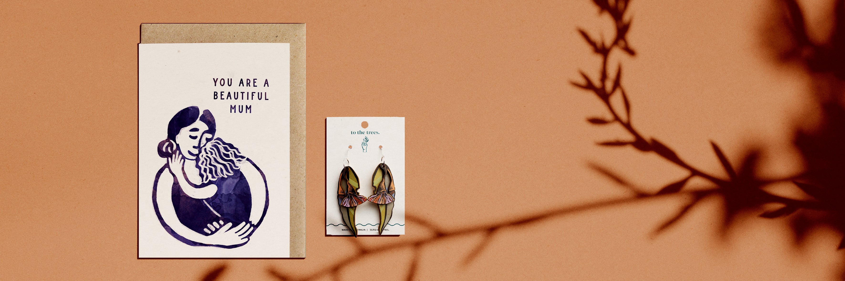 You are a beautiful mum greeting card with gum leaf and blossom earrings on a brown background with leaf shadows
